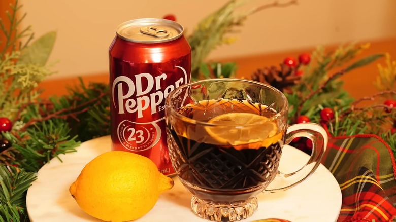 A mug of hot Dr Pepper sits on a plate with a lemon and a soda can.