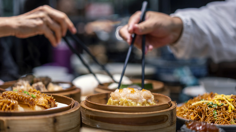 Multiple people using chopsticks to pluck food out of steamer baskets.