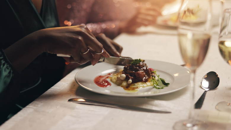 Hands holding utensils for eating food off of a plate.