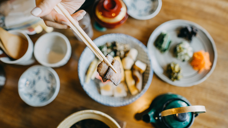 A hand uses a pair of chopsticks to lift braised meat from a traditional Japanese meal