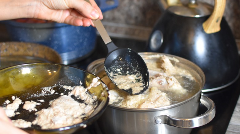 A person skimming fat from a chicken broth into a bowl