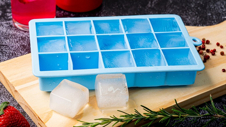 Blue ice cube tray next to two ice cubes on a wooden serving board