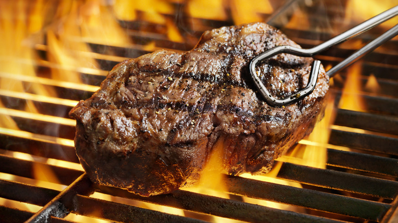 Steak being pulled from a fiery grill with grill tongs