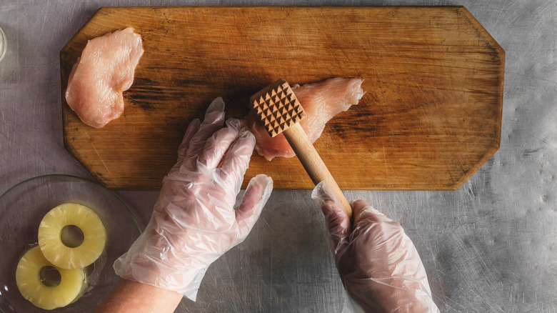 person tenderizing chicken breast with mallet