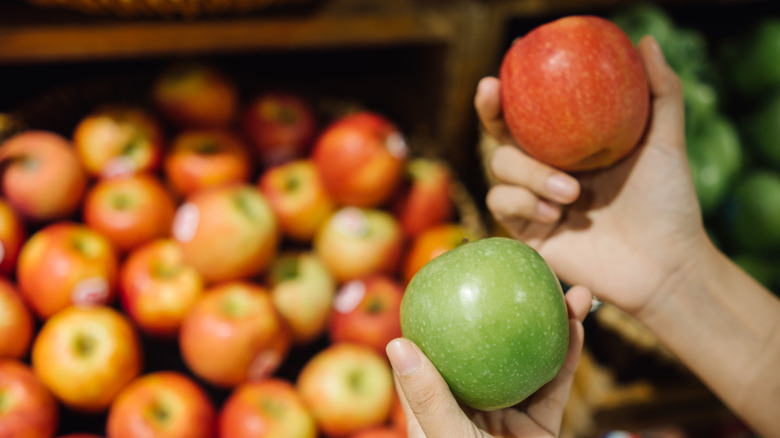 A person assessing a green and red apple at the store