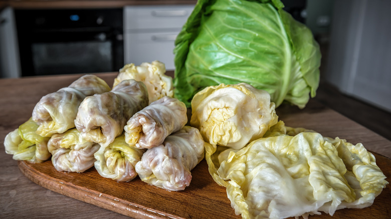 Cabbage rolls, leaves, and whole head of cabbage on wood cutting board
