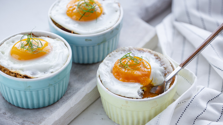 Shirred eggs in three ramekins, two blue one cream on a white surface