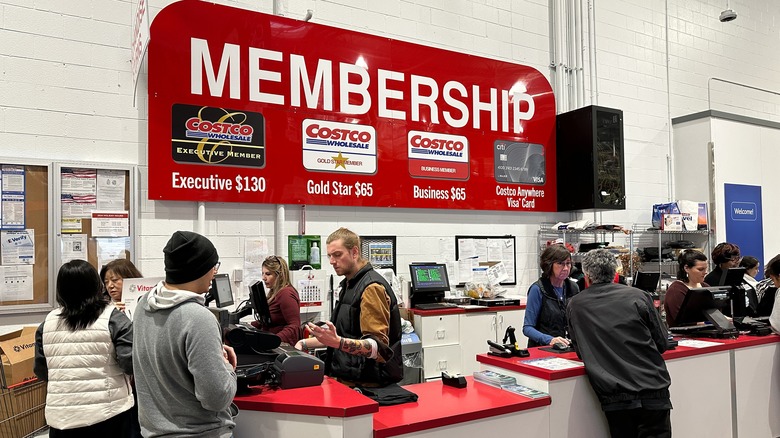 Costco employees work at a busy Costco membership counter assisting customers