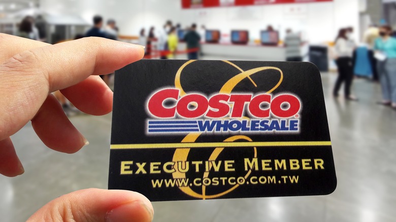 A Costco shopper holds up a black and gold executive membership card inside a Costco warehouse