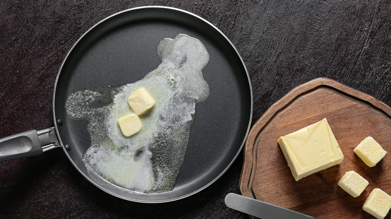 Butter melting in pan by wooden board with butter.