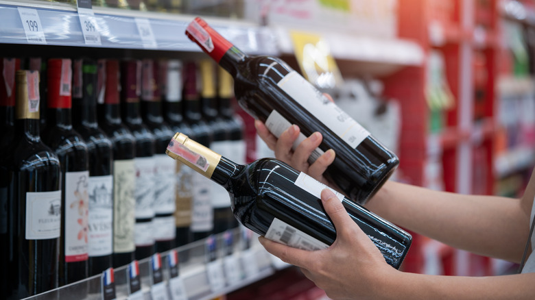 Someone choosing between two bottles of wine in a wine shop.