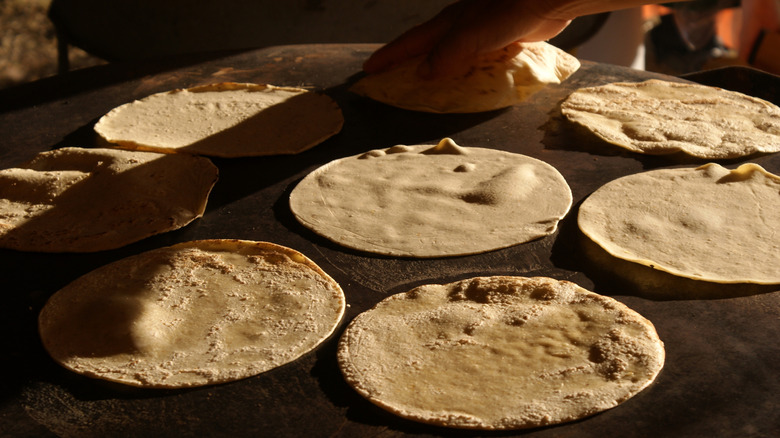 Eight partially cooked flour tortillas being warmed on a hot stone