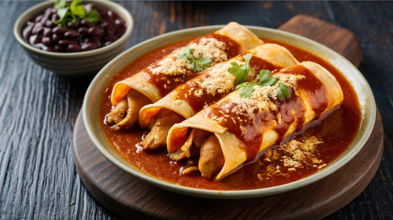 A plate of chicken enchiladas covered in red sauce with a side of black beans