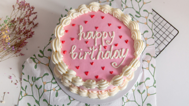 A round, pink cake has "happy birthday" written in white frosting.