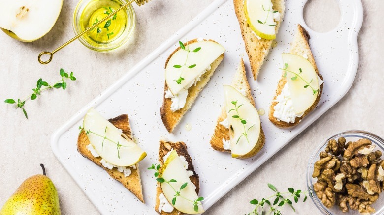 Brie and sliced pears on bread slices on a white serving tray 