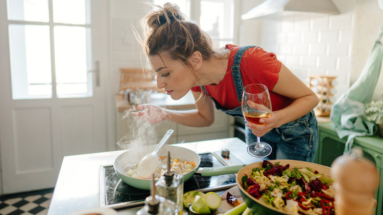 young woman cooking with glass of wine in her hand