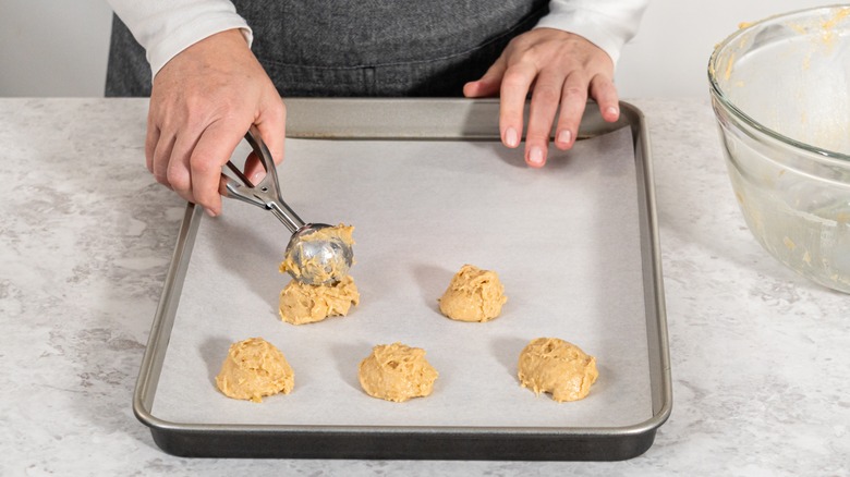 woman scooping cookie dough on parchment lined sheet pan