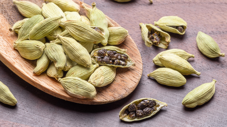 Closed and opened cardamom pods on a wooden surface