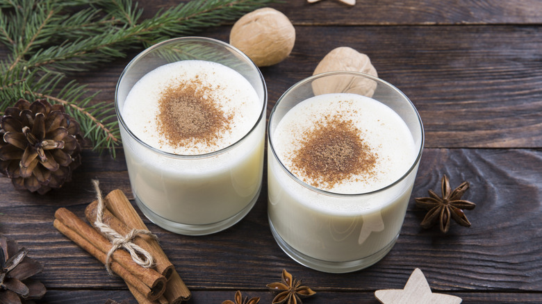 Two glasses of holiday eggnog sprinkled with nutmeg sit beside whole spices