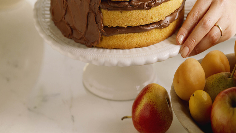 Hand frosting a yellow layered cake with chocolate frosting