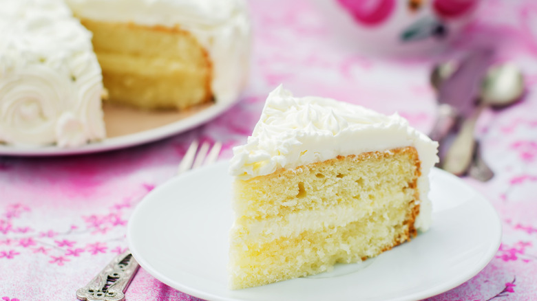 Slice of vanilla cake with white frosting on pink tablecloth