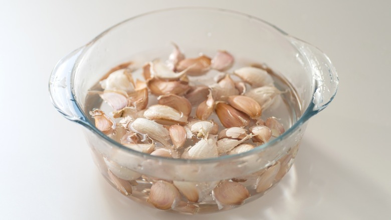 Many cloves of garlic in a clear glass bowl of water