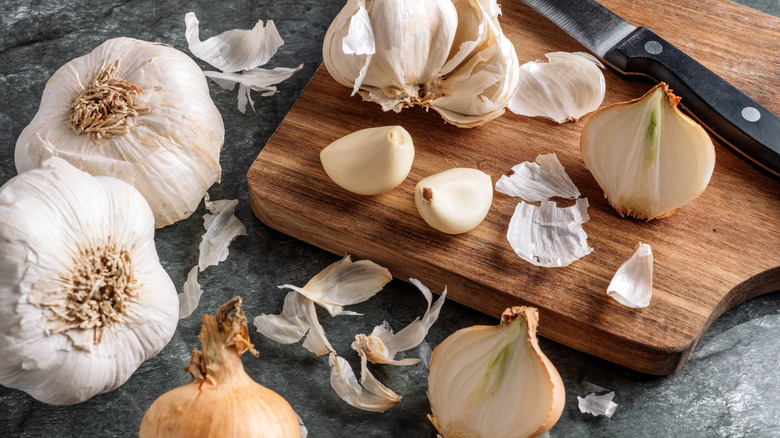 Garlic bulbs, cloves, and peels on wood cutting board with knife