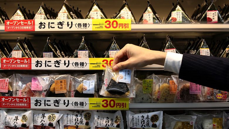 Hand arranging onigiri on display in a Japanese konbini