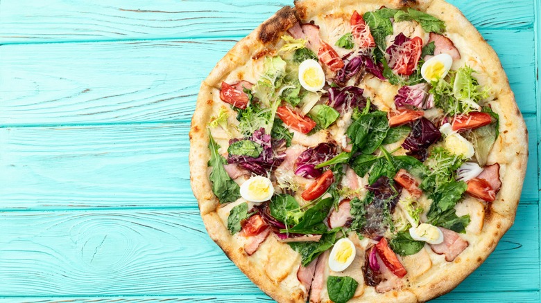 A pizza crust topped with lettuce, hard-boiled eggs, and other salad ingredients