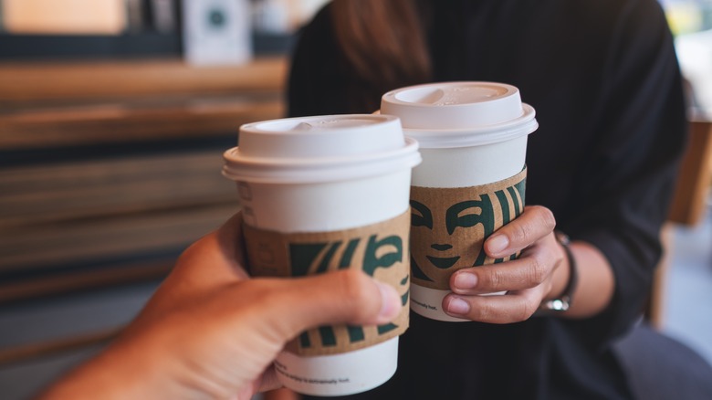 Two people holding Starbucks coffee cups