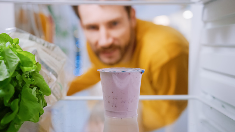 Man looks at purple yogurt in fridge