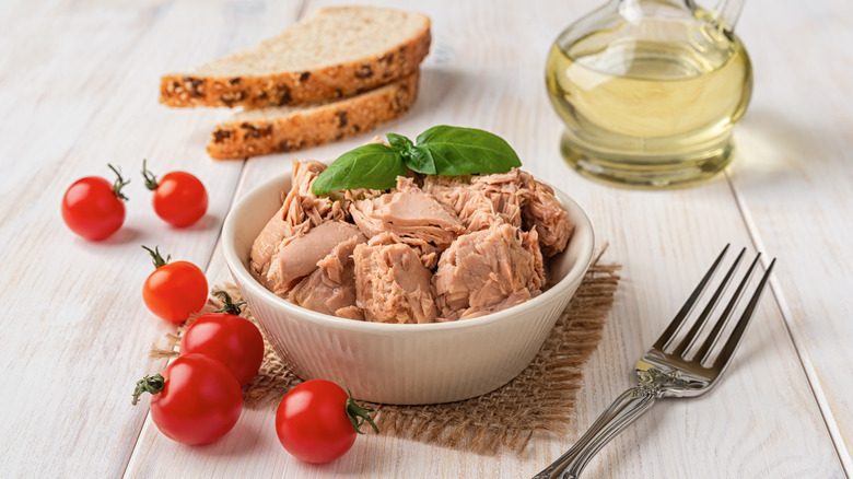bowl of canned tuna alongside some rye bread, tomatoes, and oil