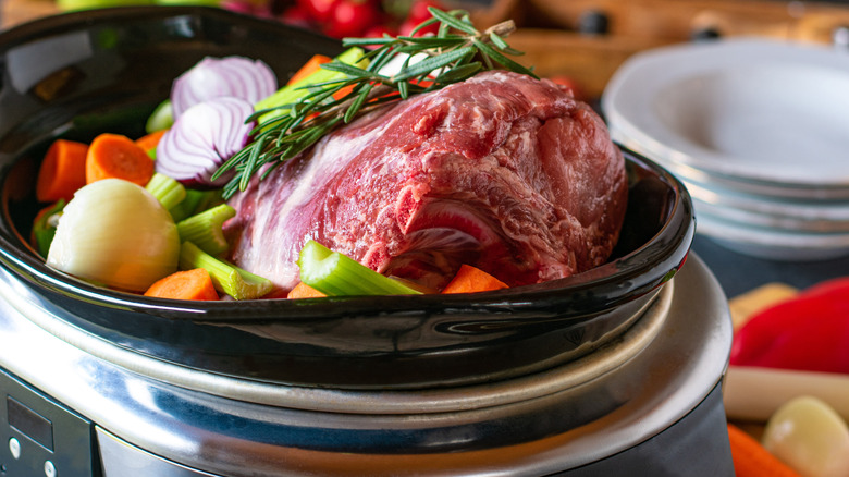 A raw roast sits with vegetables in a slow cooker