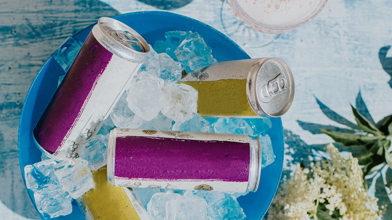 Metal drink cans in a blue bowl filled with ice cubes