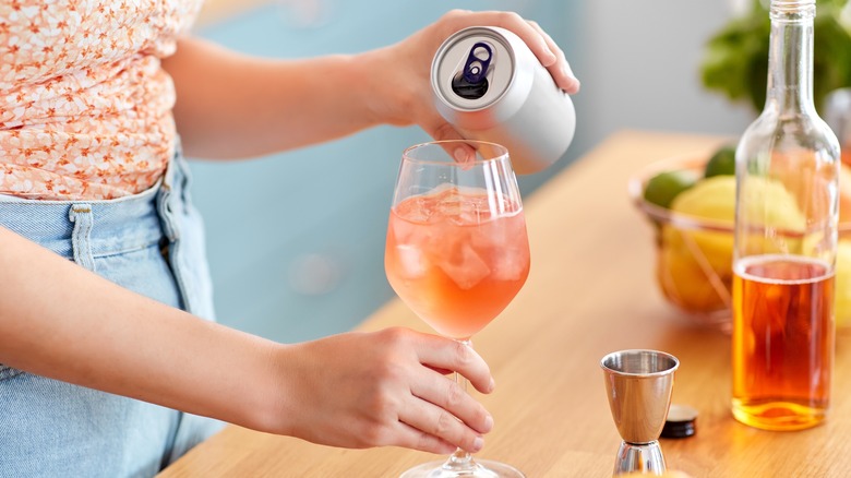 Can of drink being poured into a wine glass with ice