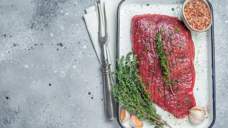 Flank steak with herbs and garlic on a white dish with a metal serving fork.