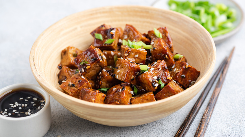 Fried teriyaki tofu cubes in bowl with chopsticks and sauce