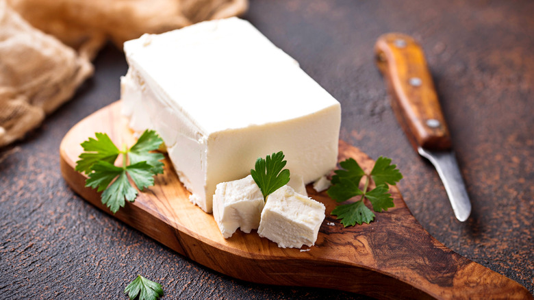 A black of feta cheese on a cutting board next to a knife