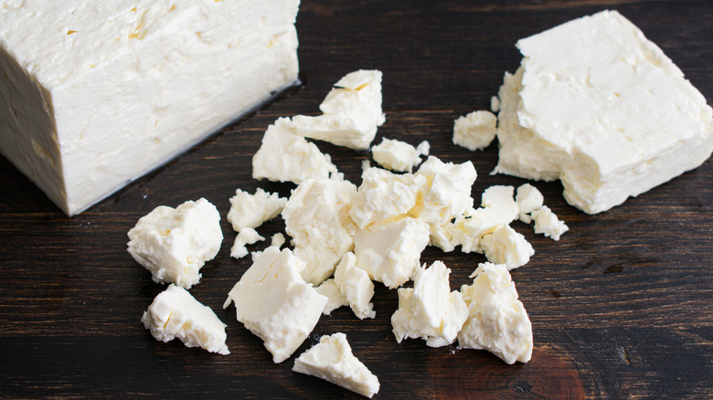 Chunks and whole cubes of feta cheese on a wooden surface