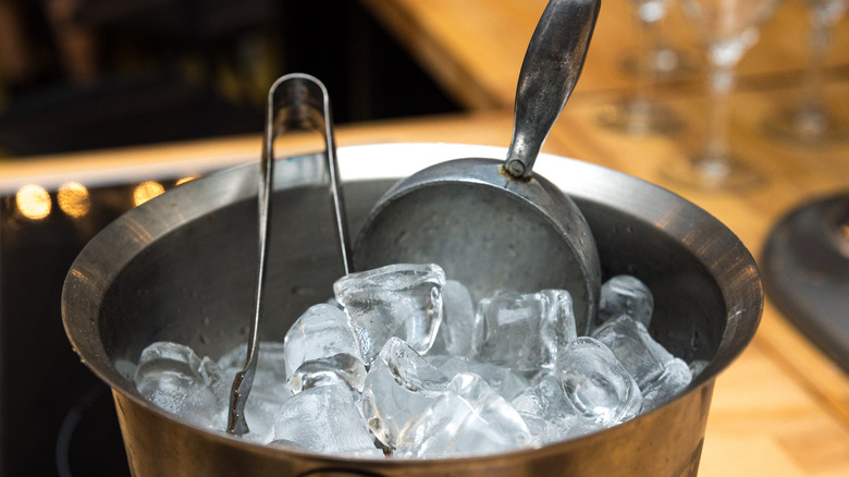 Metal ice bucket filled with frozen cubes scoop and tongs