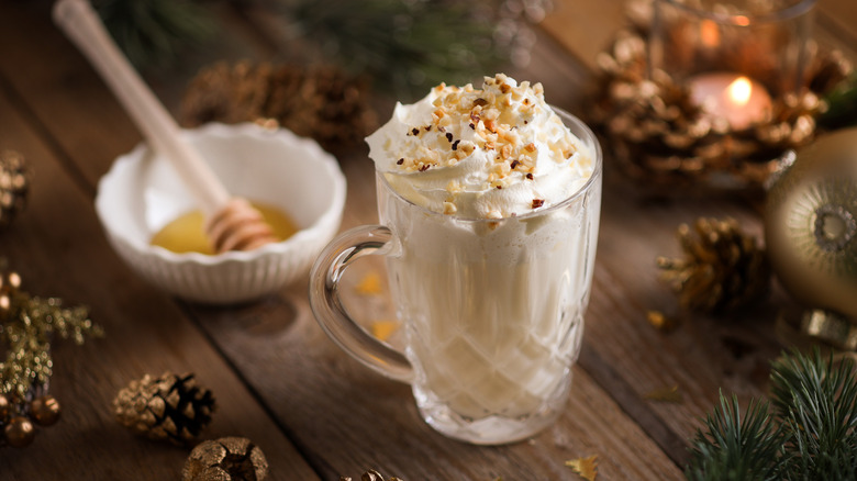 Eggnog latte in glass mug topped with whipped cream and nuts