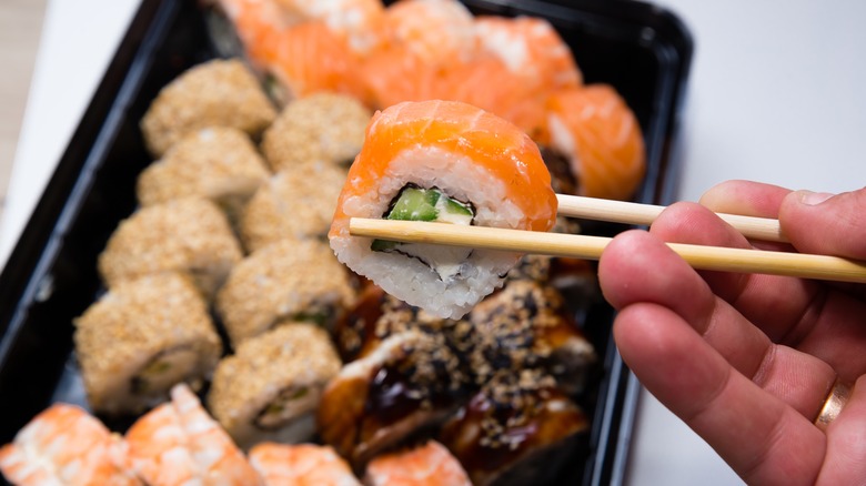 Person holding a piece of sushi with chopsticks