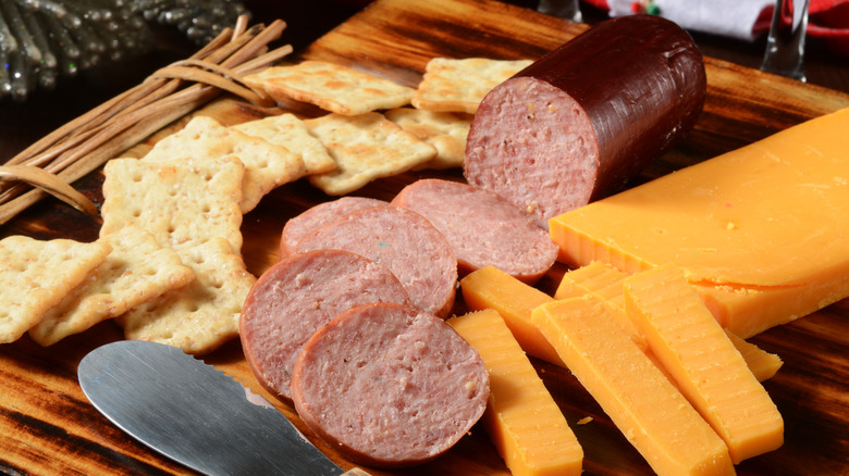 A charcuterie board with crackers, cheddar cheese, and summer sausage