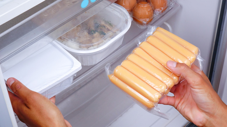 person putting vacuum sealed hot dogs in the fridge