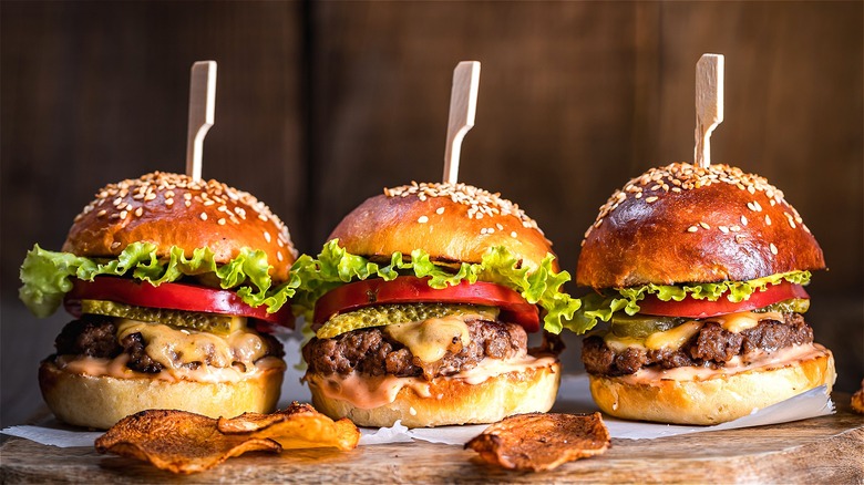 Three cheeseburgers with lettuce, tomato, and pickles