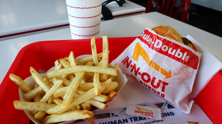 A tray with In-N-Out french fries and a Double-Double Burger, with a drink in the background