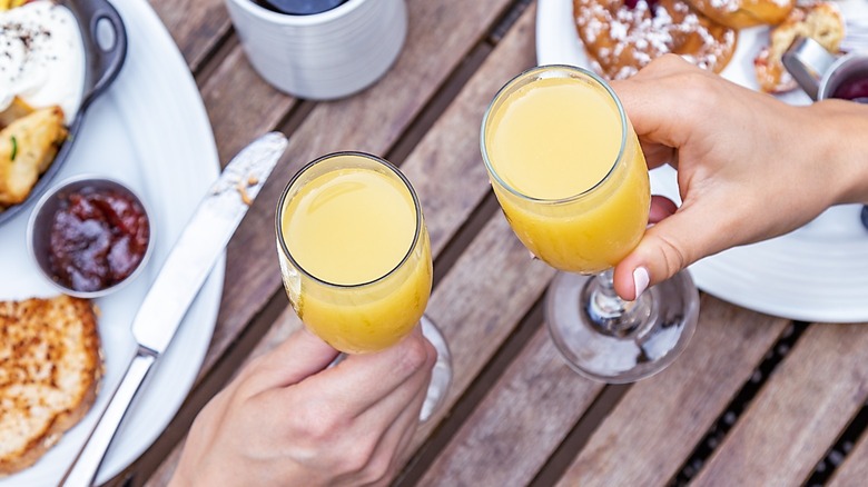 Two people holding mimosas over breakfast foods