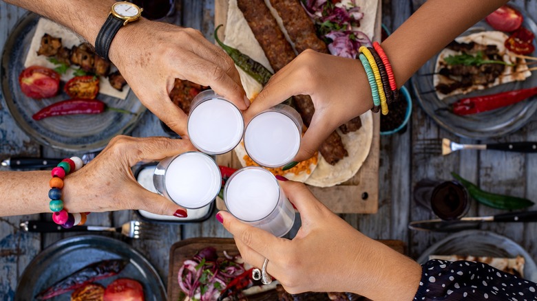 Four hands toasting with arak over table