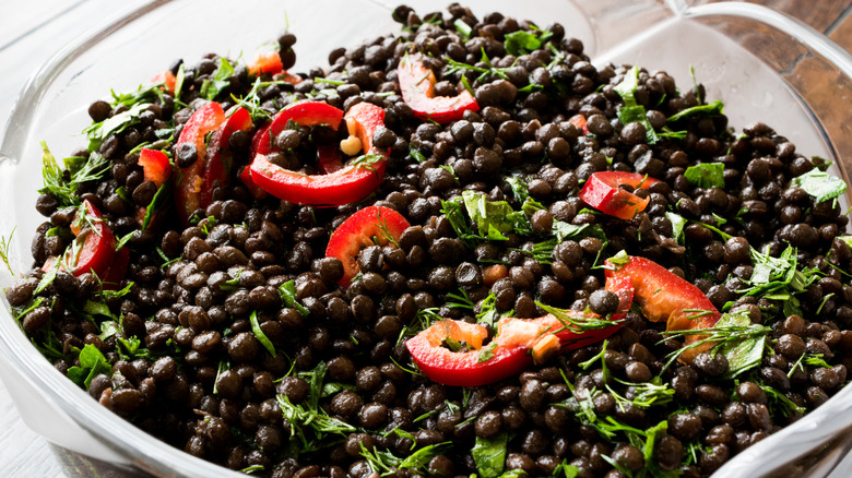 Black lentil salad with greens and peppers in clear bowl