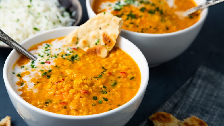 Red lentil curry with spices and naan in white bowl